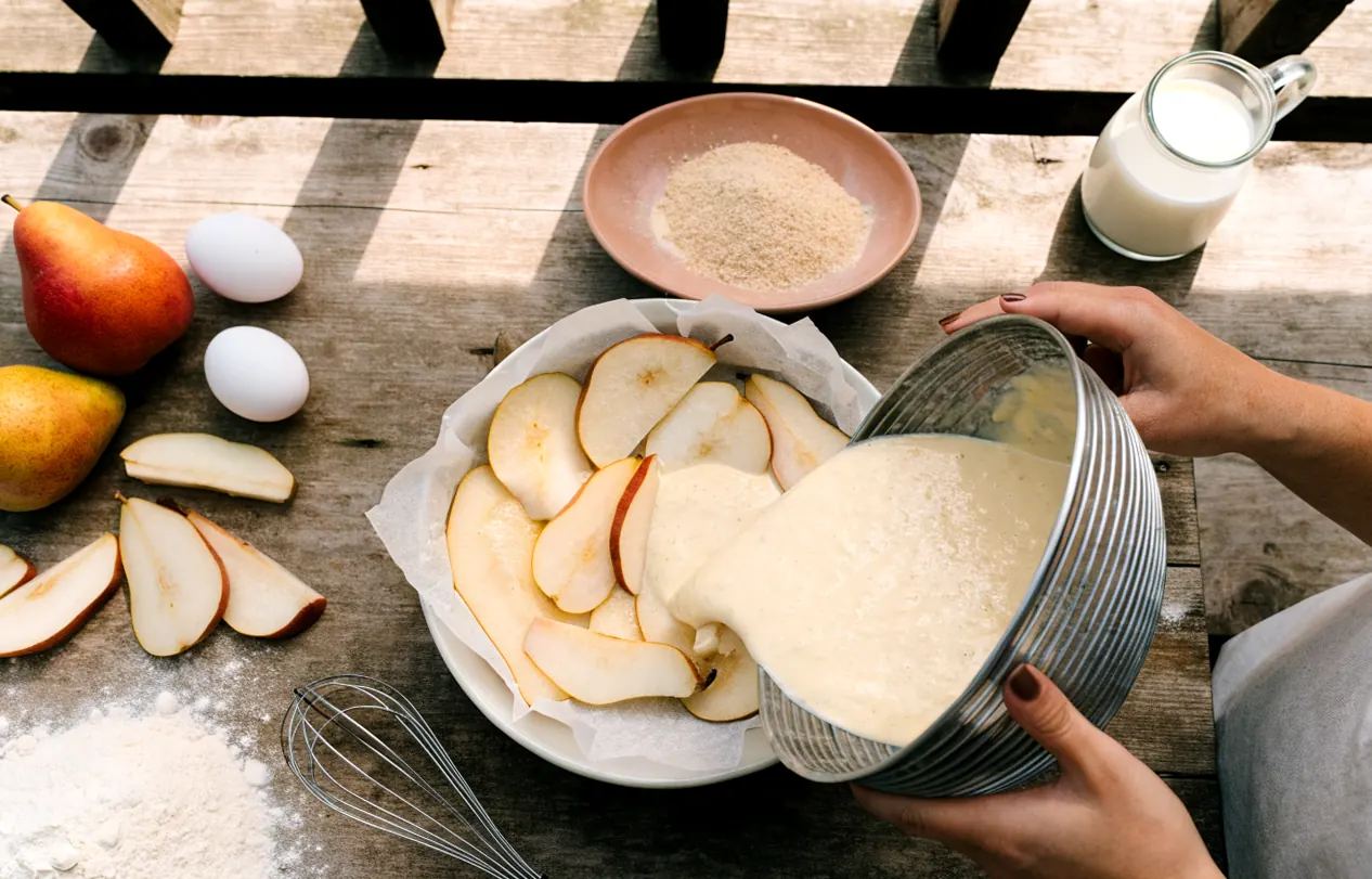 Préparation du clafoutis sans beurre : pâte au lait versée sur les poires dans le moule chemisé