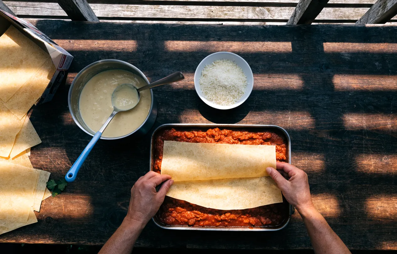Montaje de las láminas de lasaña sobre el ragú y la bechamel en una fuente para horno, vista desde arriba