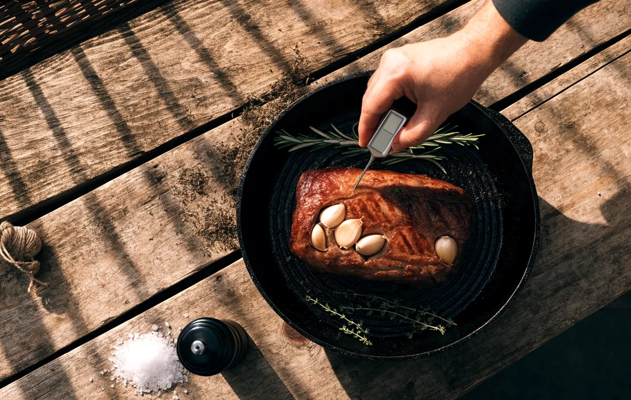 Contrôle de la cuisson du rosbeef au thermomètre dans une cocotte en fonte avec ail et herbes