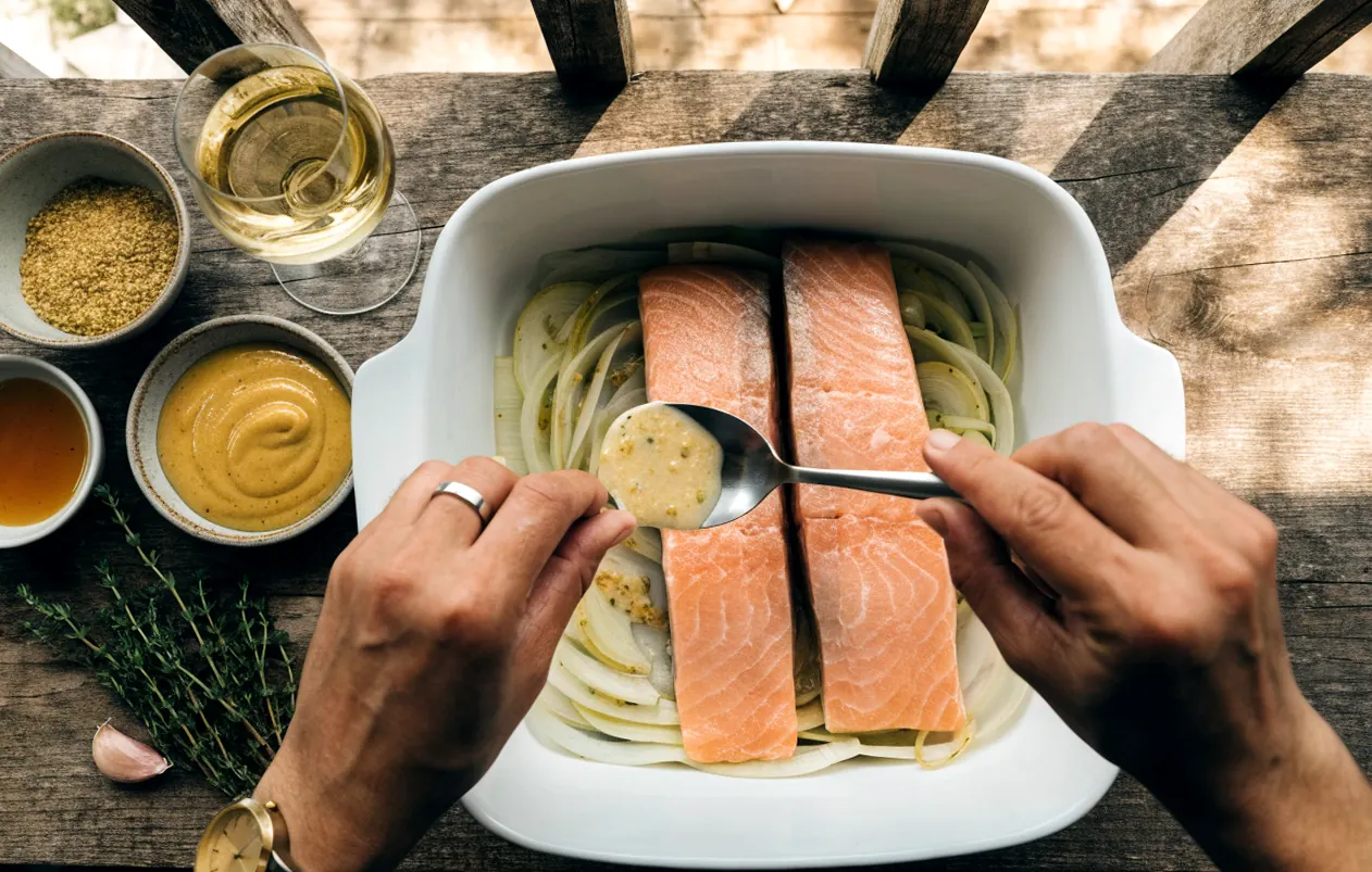 Preparing the sauce for baked salmon: pour mustard, honey, and white wine over the raw salmon fillets