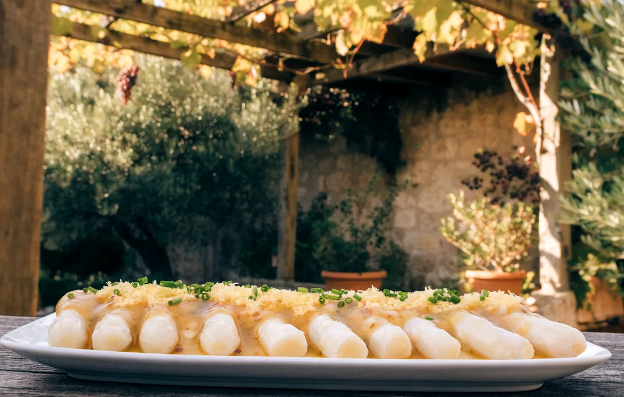 Asperges blanches à la vinaigrette mimosa, œuf râpé et ciboulette, sous une pergola en bois couverte de vigne