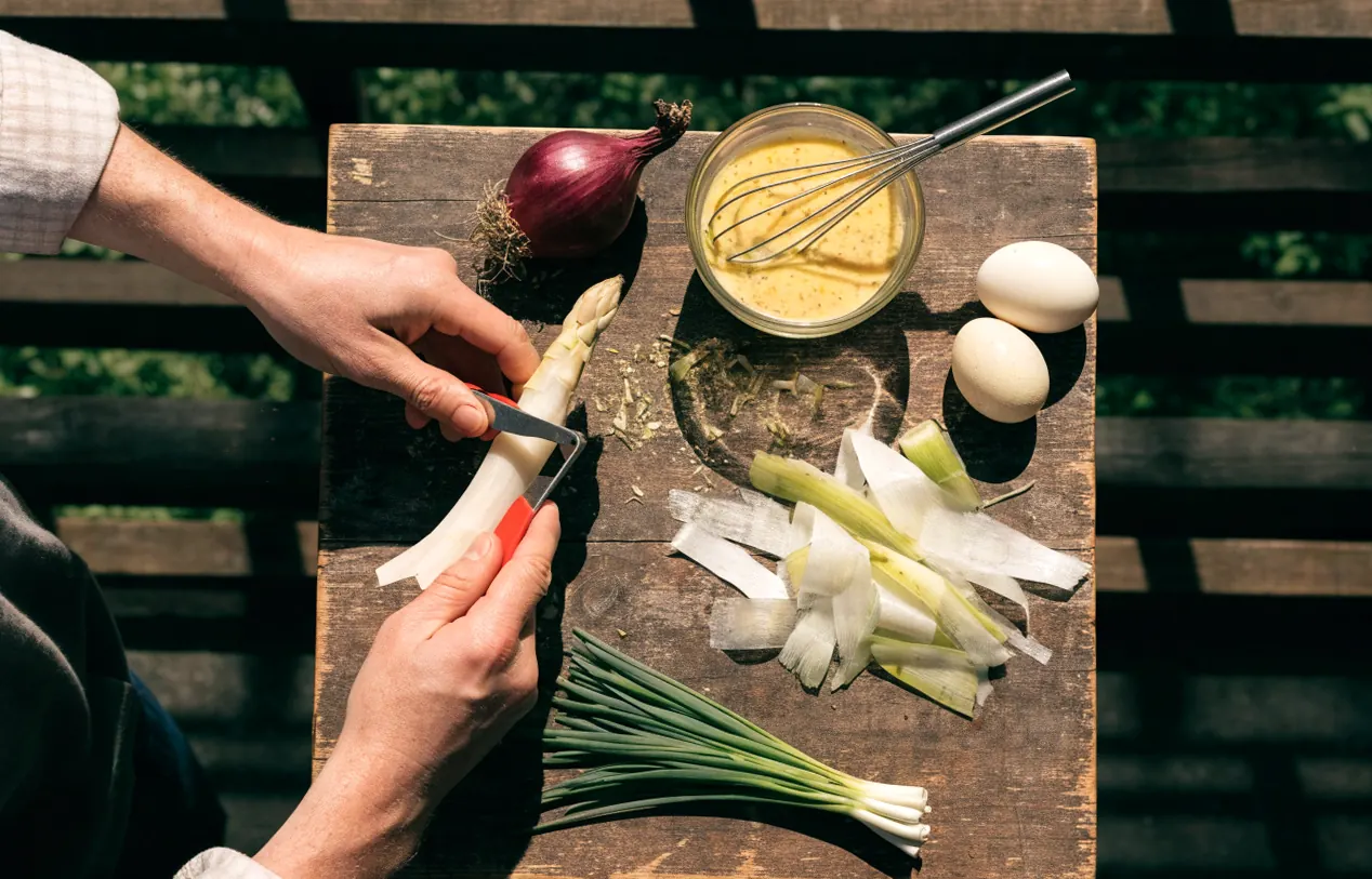 Épluchage des asperges blanches et vinaigrette à la moutarde préparée sur une table rustique